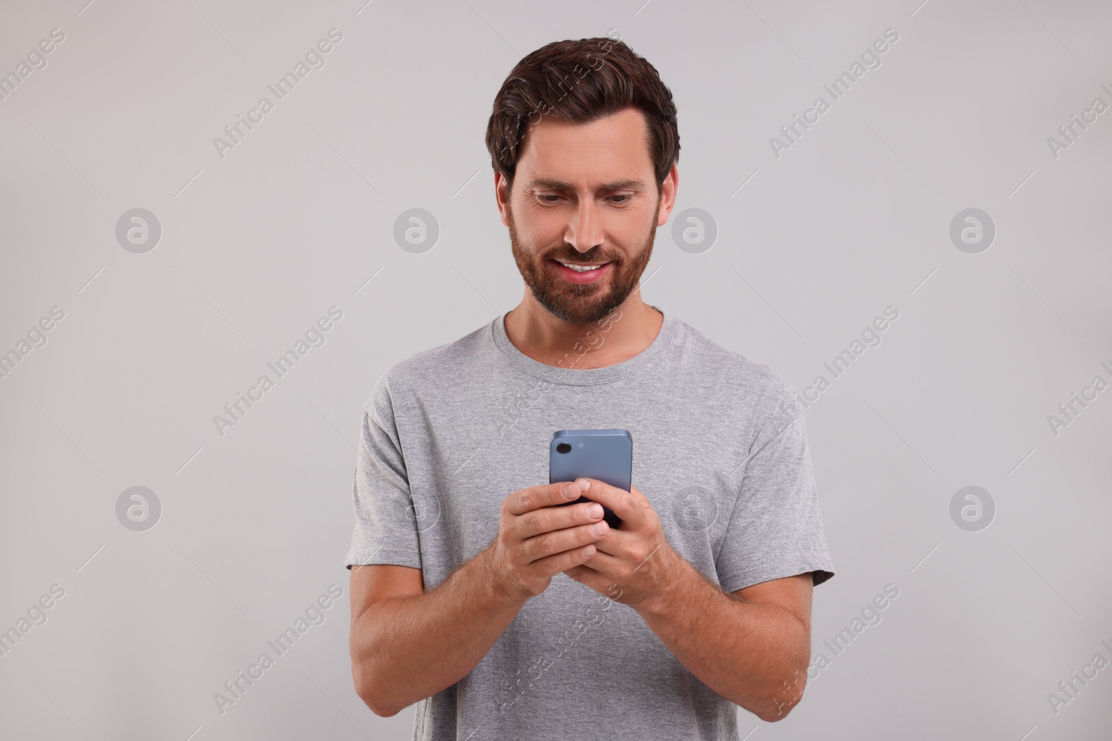 Photo of Handsome bearded man using smartphone on grey background