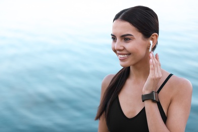 Photo of Young sportswoman with wireless earphones near river
