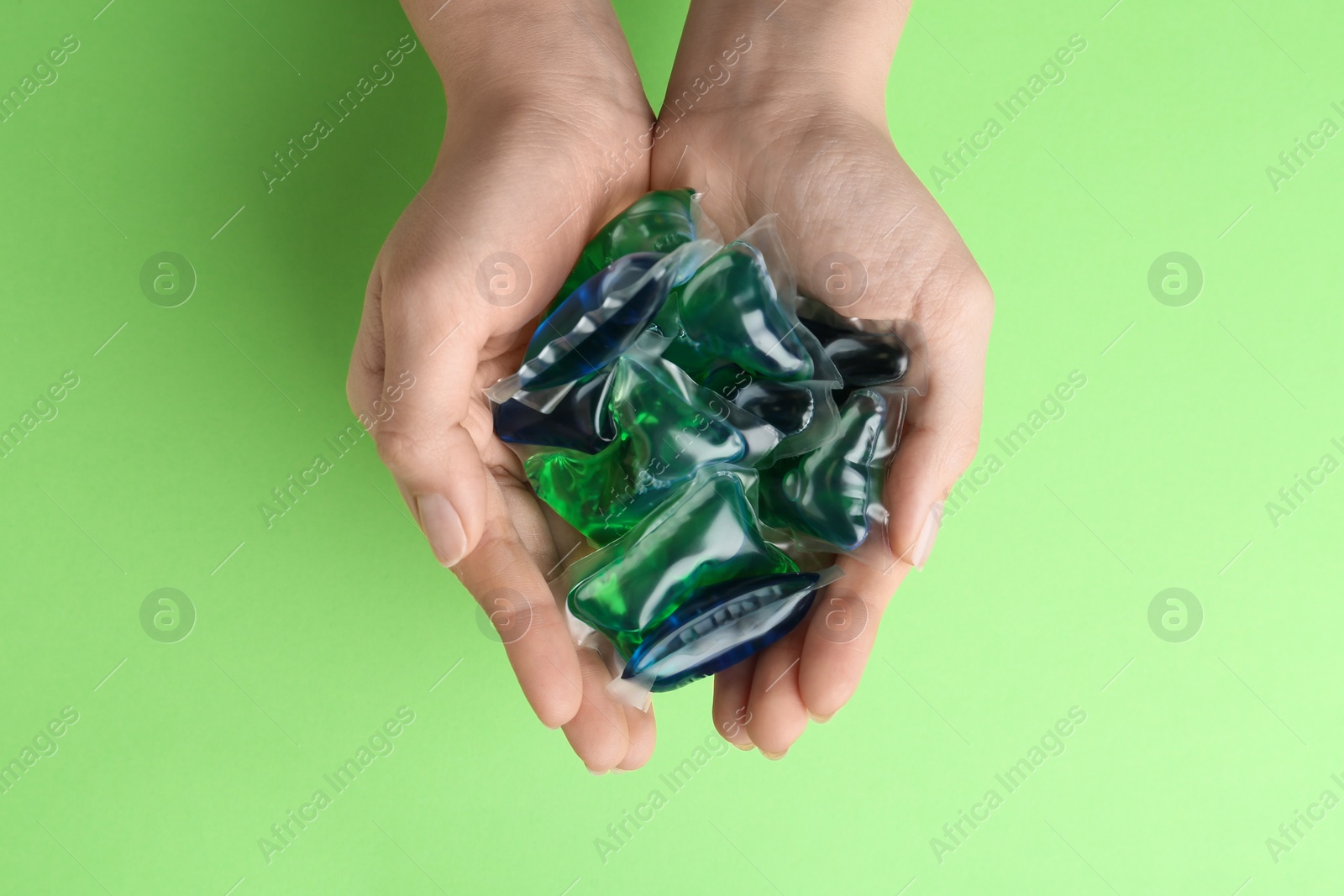 Photo of Woman holding laundry capsules on green background, top view
