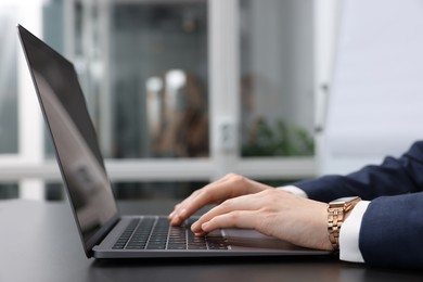 Photo of Woman working with laptop at black desk in office, closeup