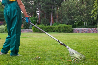 Photo of Woman raking green lawn at backyard. Home gardening