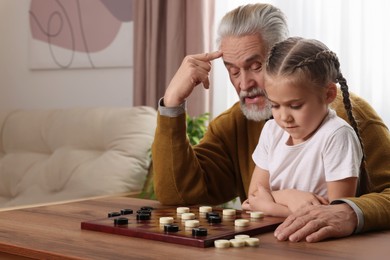 Playing checkers. Grandfather learning little girl at table in room