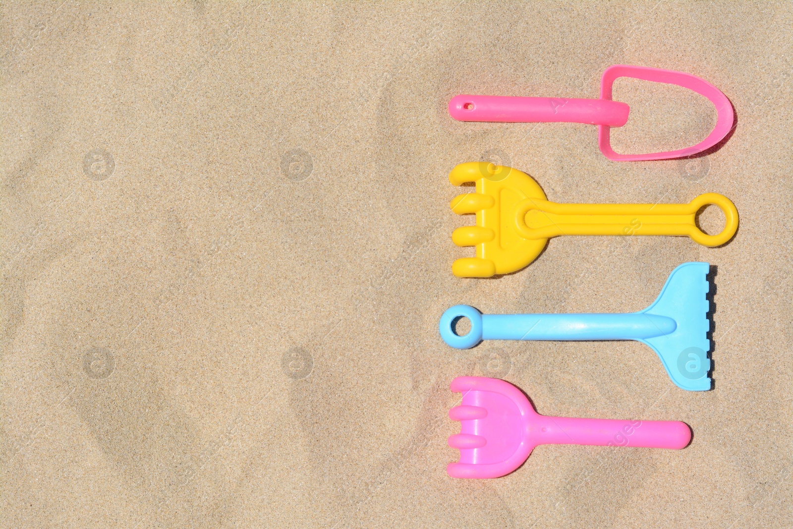 Photo of Bright plastic rakes and shovel on sandy beach, flat lay. Space for text