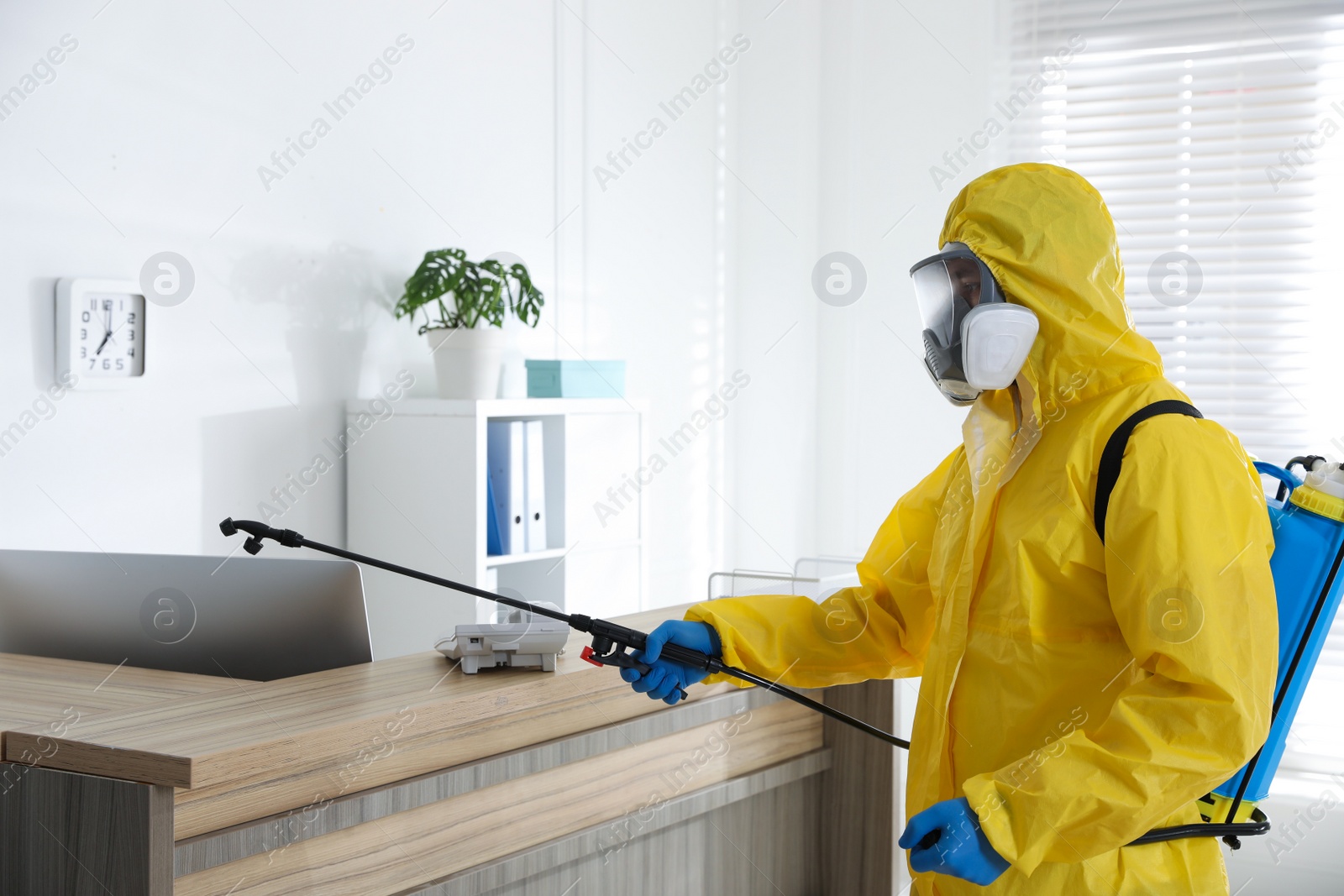 Photo of Employee in protective suit sanitizing office. Medical disinfection