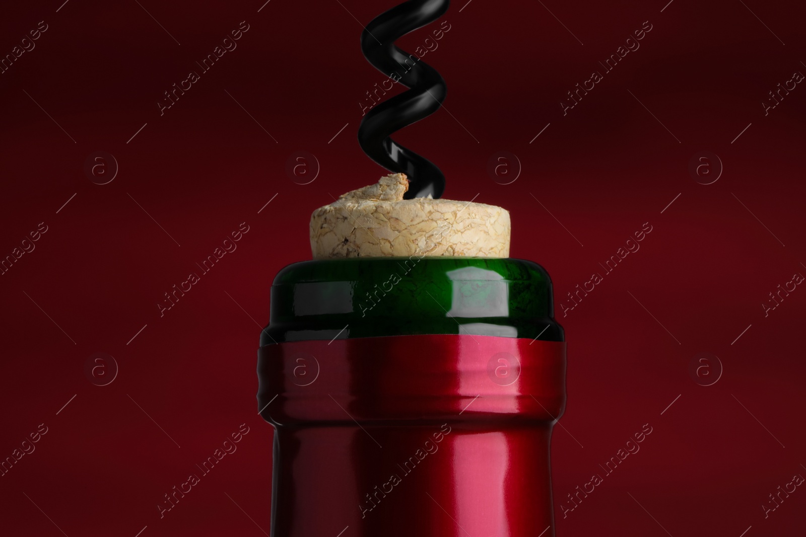 Photo of Opening bottle of wine with corkscrew on burgundy background, closeup