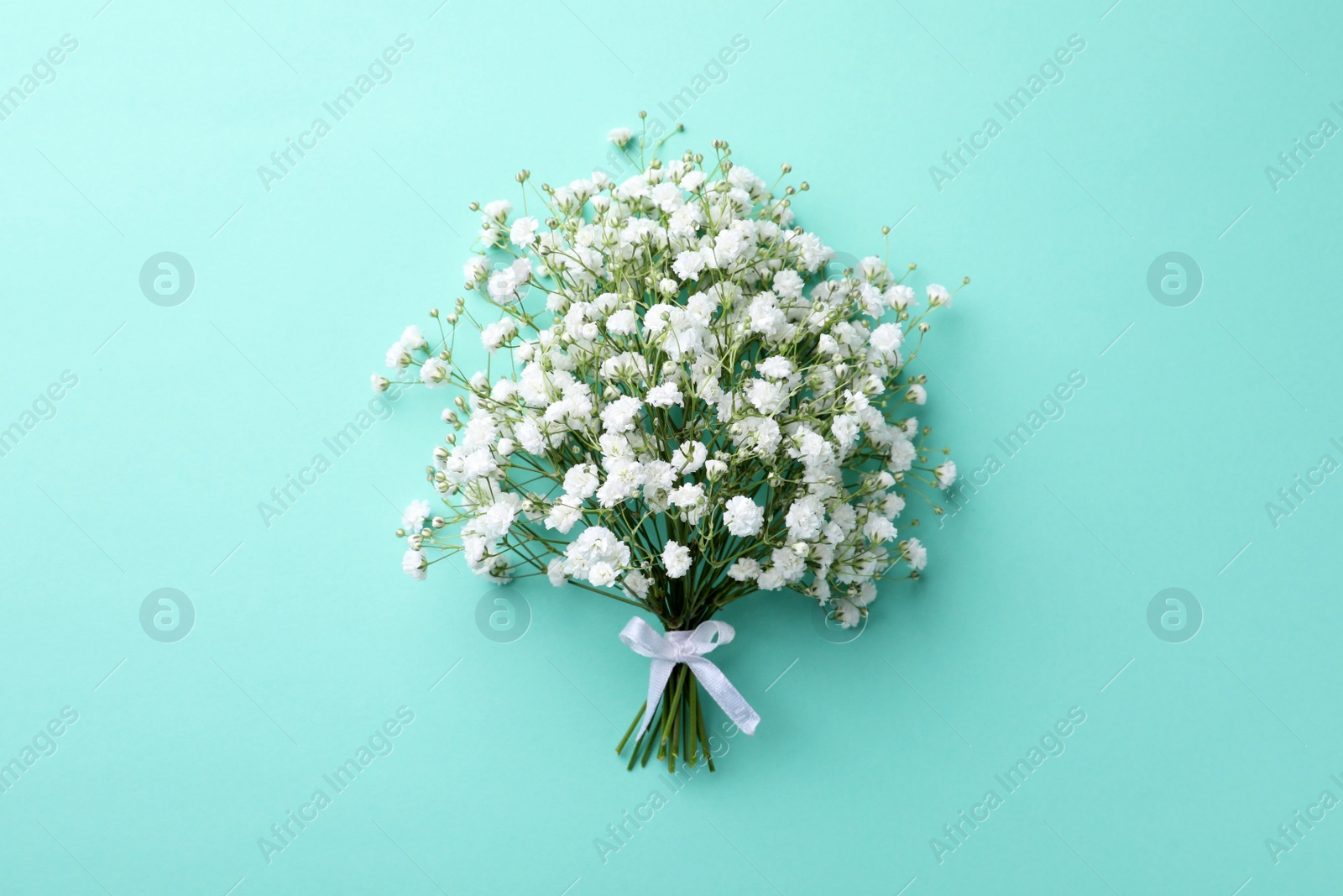 Photo of Beautiful gypsophila flowers tied with ribbon on turquoise background, top view