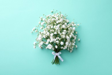 Beautiful gypsophila flowers tied with ribbon on turquoise background, top view