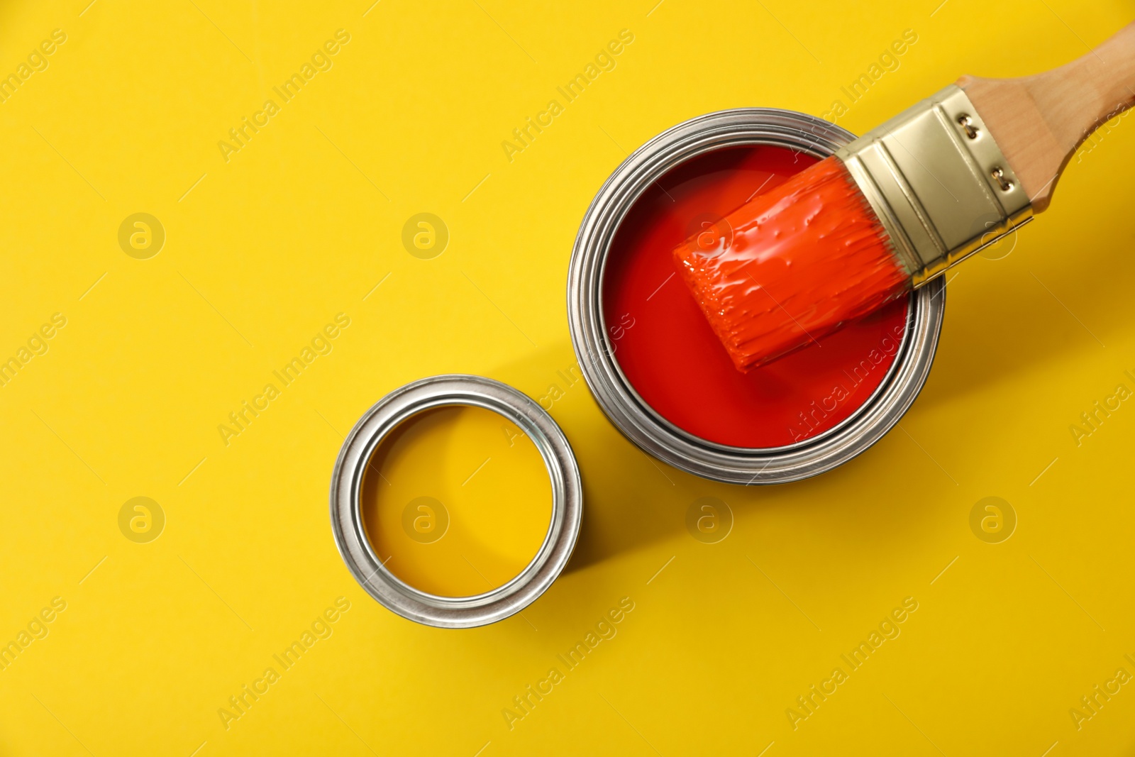 Photo of Cans of different paints and brush on yellow background, flat lay