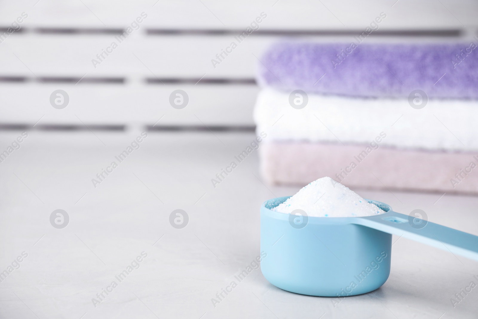 Photo of Clean towels and measuring scoop of washing powder on table. Space for text