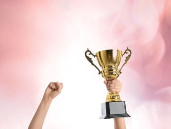 Woman holding gold trophy cup on color background, closeup