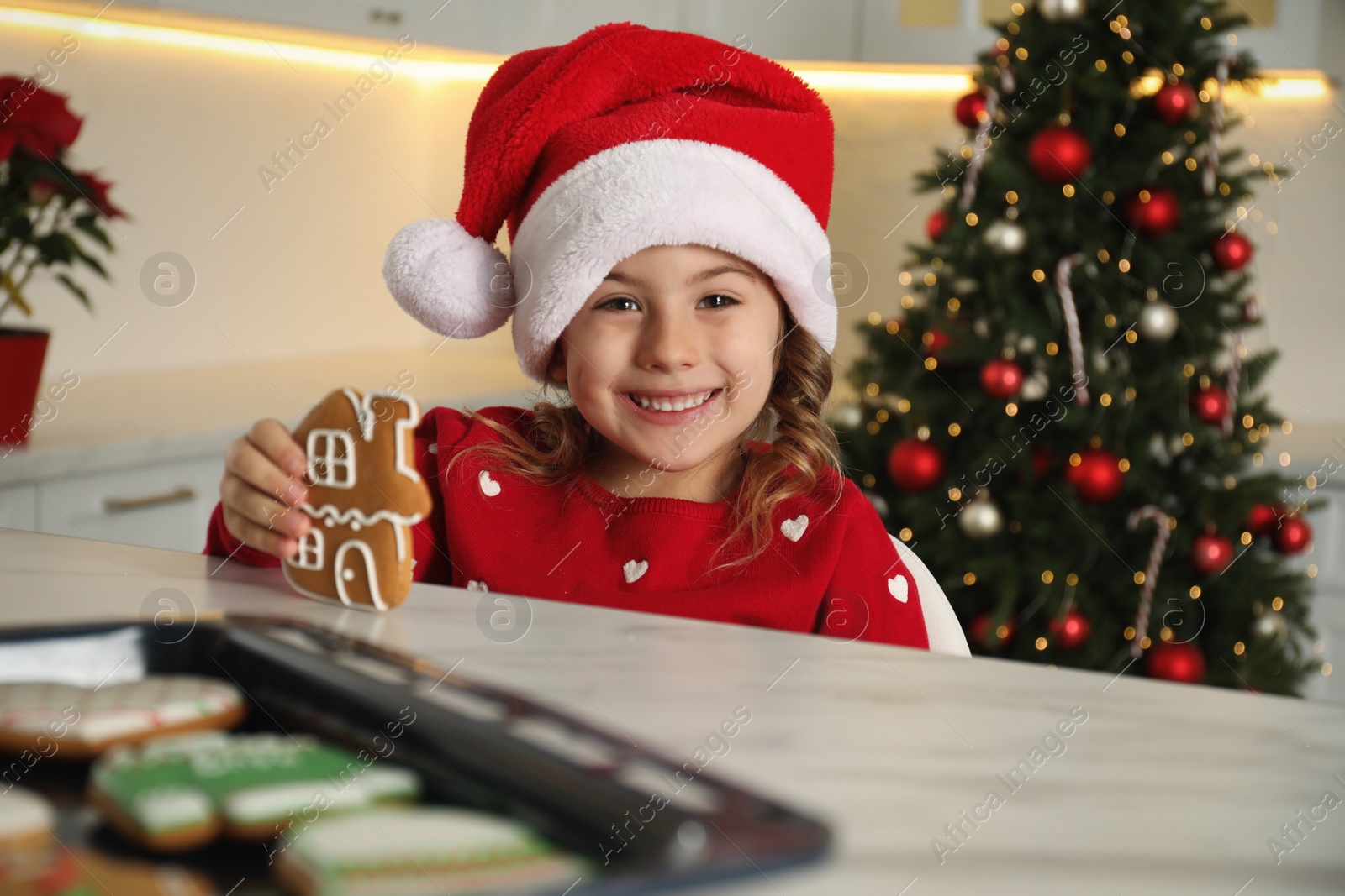 Photo of Cute little girl with freshly baked Christmas gingerbread cookie at table indoors