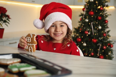 Cute little girl with freshly baked Christmas gingerbread cookie at table indoors