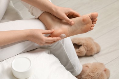 Photo of Young woman with dry skin applying cream onto her foot indoors, closeup