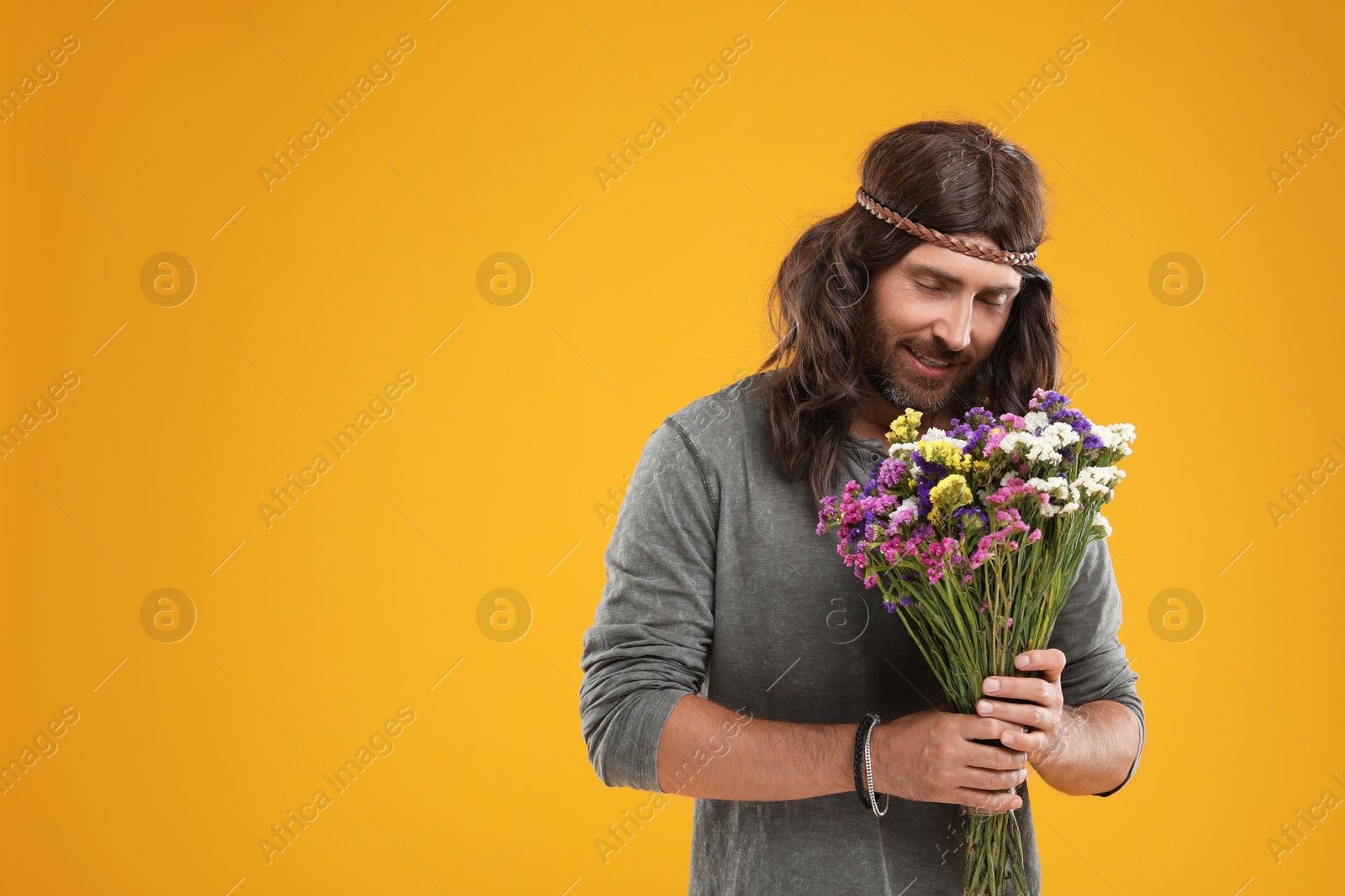 Photo of Hippie man with bouquet of colorful flowers on orange background, space for text