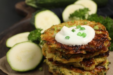 Photo of Delicious zucchini fritters with sour cream on board, closeup