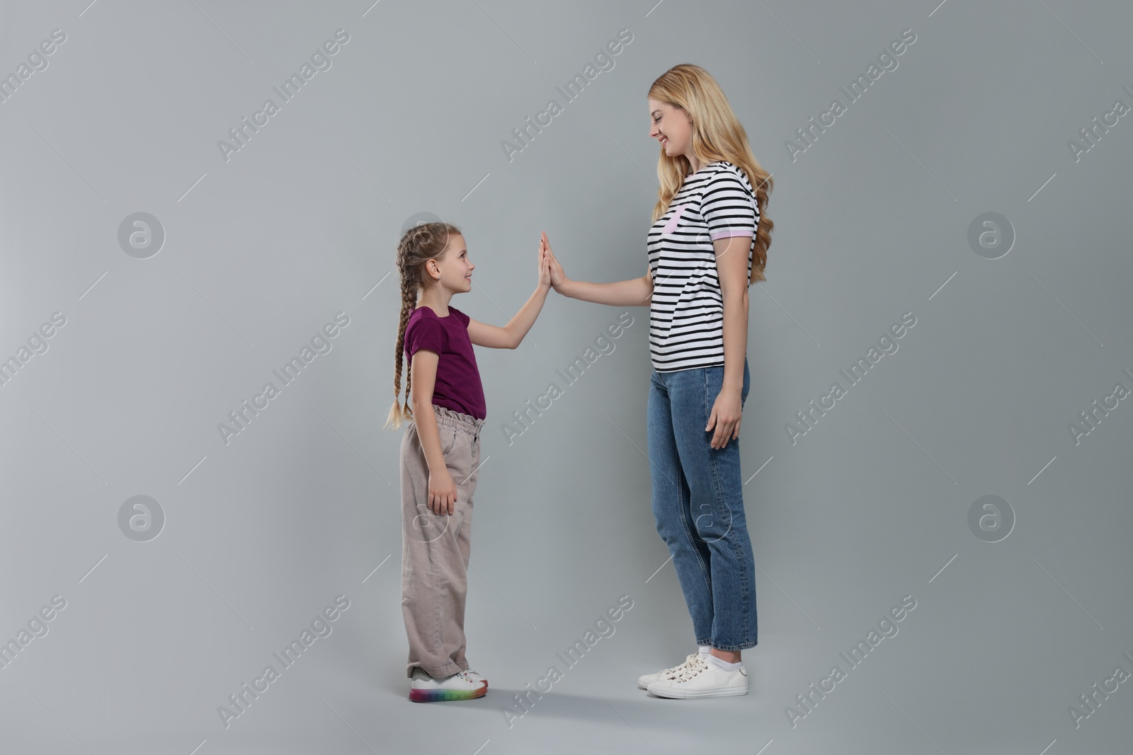 Photo of Mother and daughter giving high five on light grey background