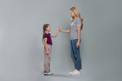 Mother and daughter giving high five on light grey background