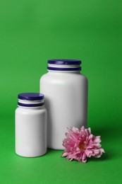 Photo of Medicine bottles and pink flower on green background. Medicament