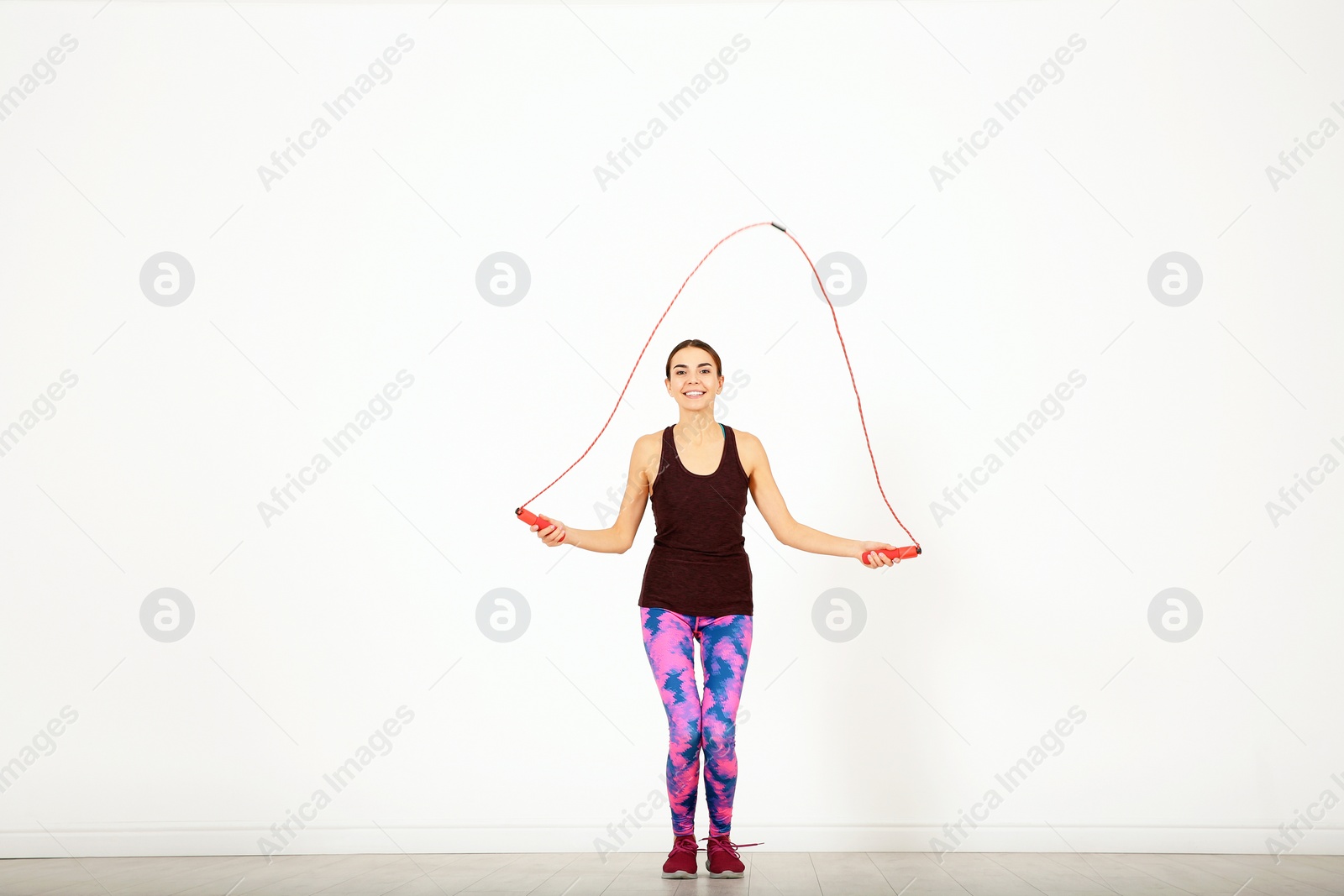 Photo of Full length portrait of young sportive woman training with jump rope in light room