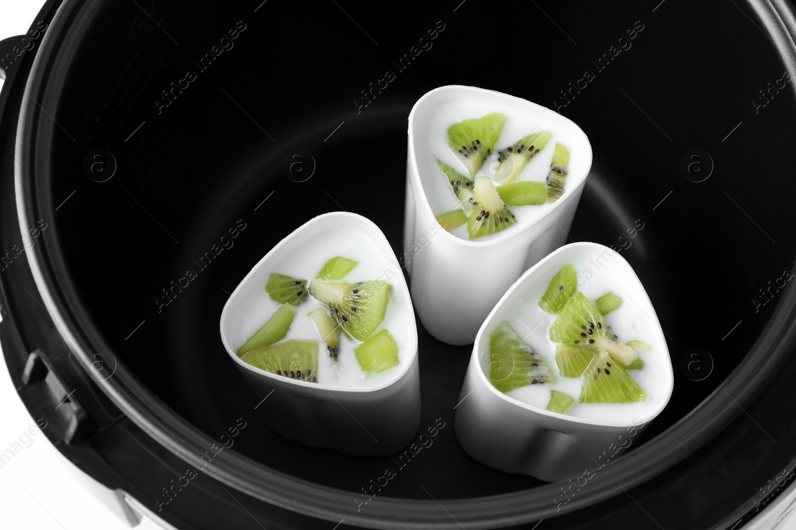 Photo of Cups of homemade kiwi yogurt in modern multi cooker, closeup view