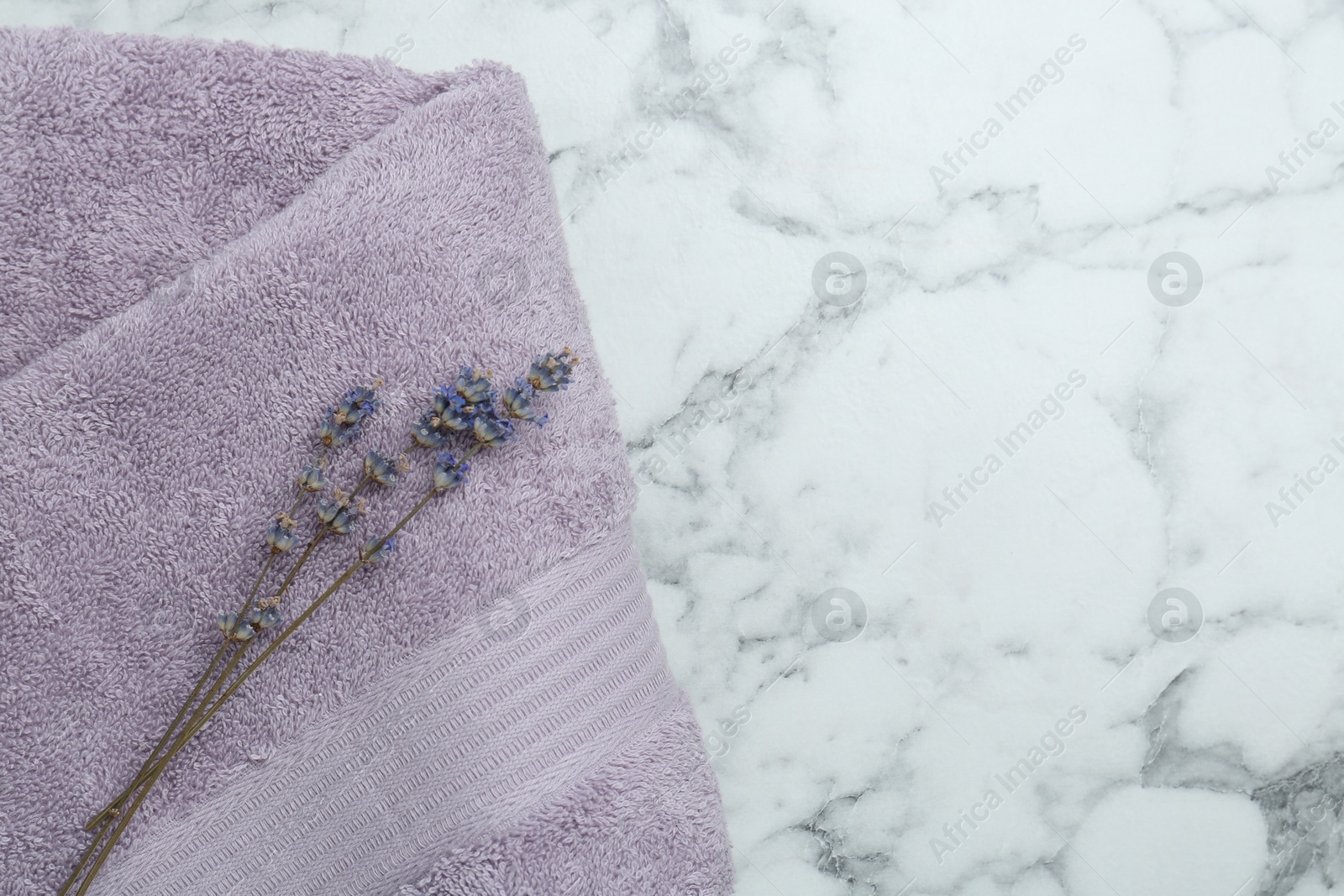 Photo of Violet terry towel and dry flowers on white marble table, top view. Space for text