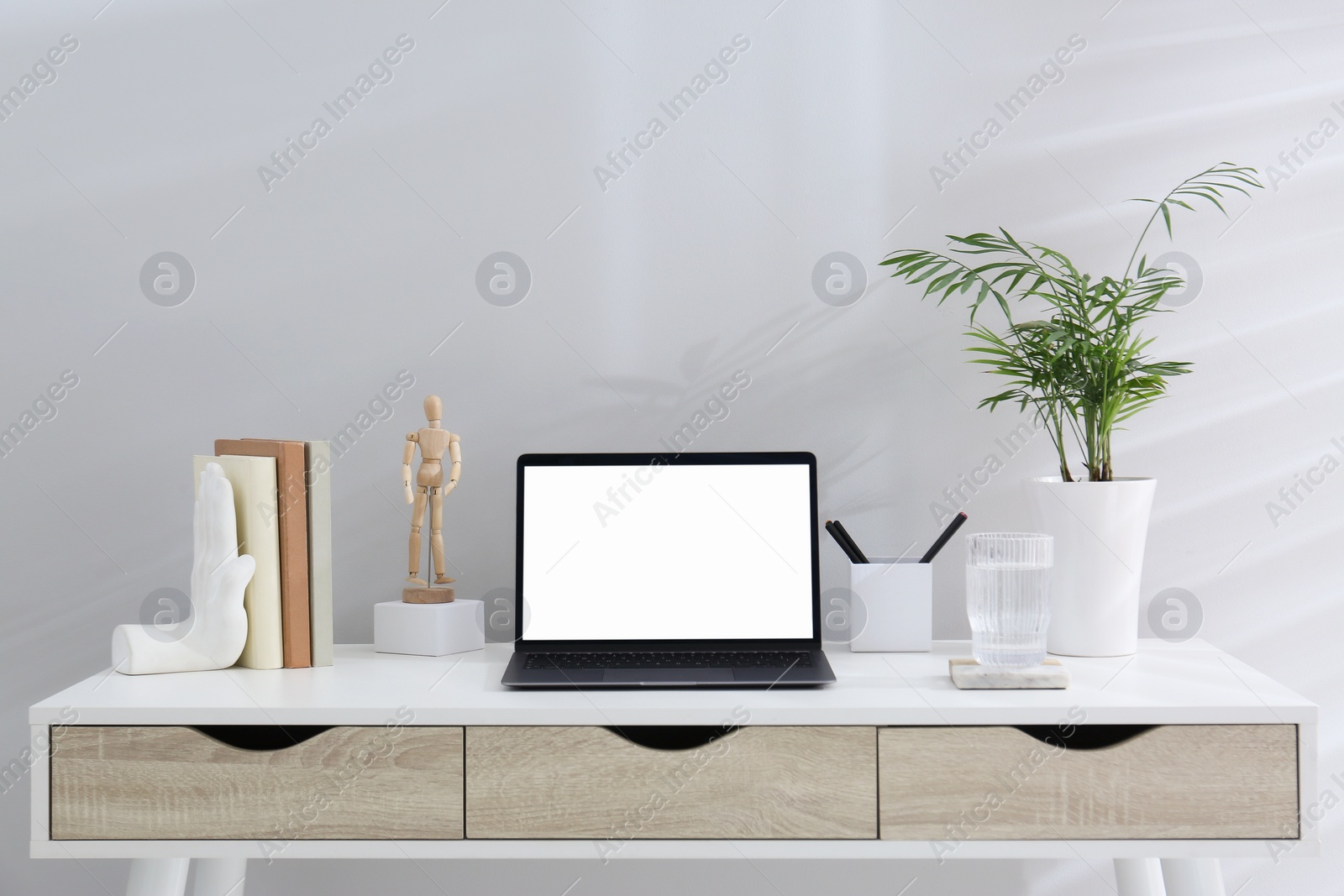 Photo of Stylish workplace with laptop, houseplant and stationery on wooden table near white wall