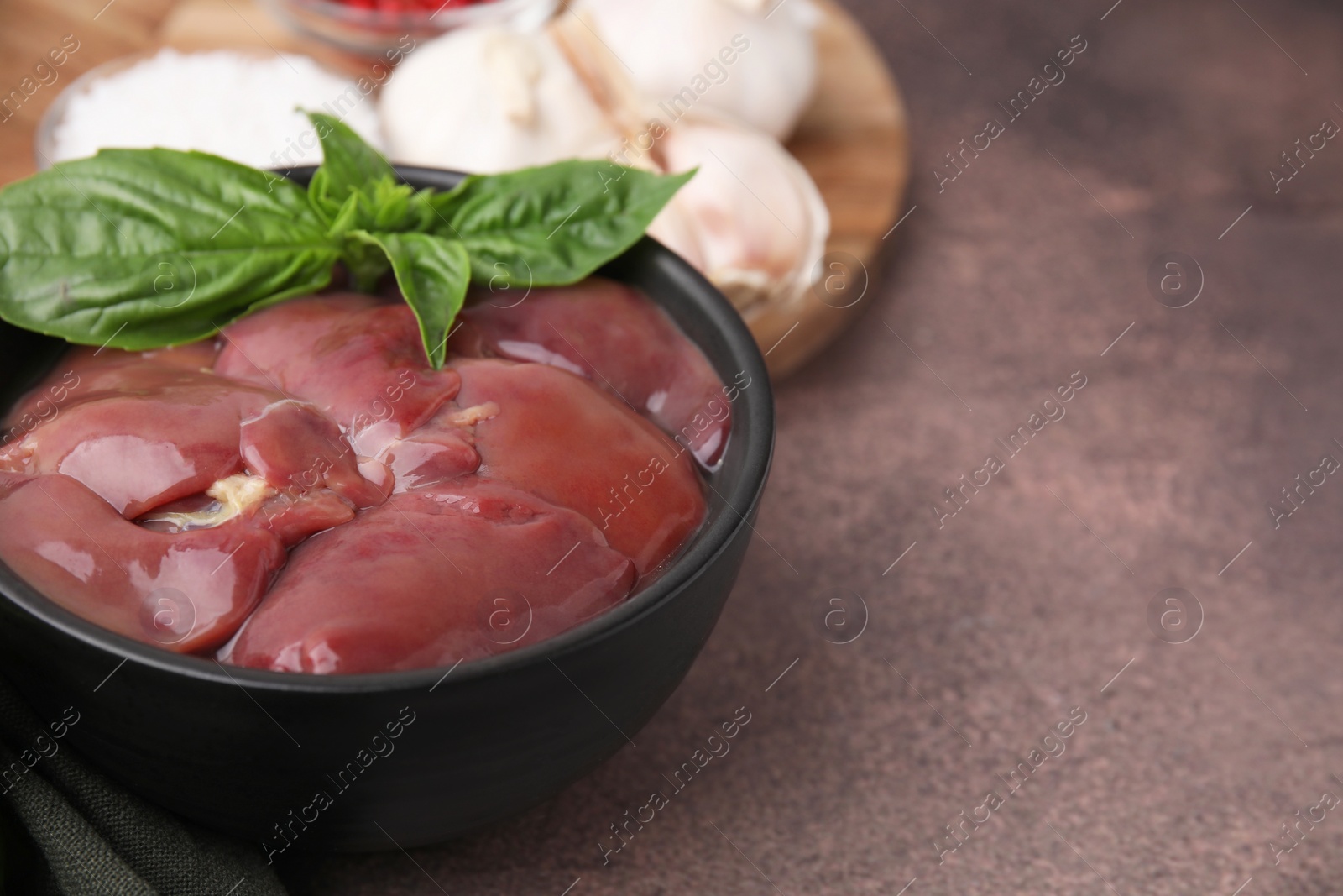 Photo of Bowl of raw chicken liver with basil on grey table, closeup. Space for text