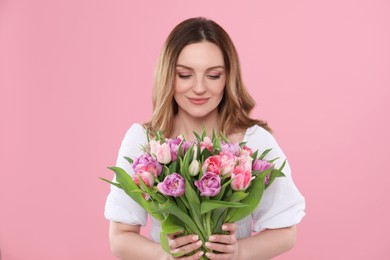 Happy young woman with bouquet of beautiful tulips on pink background