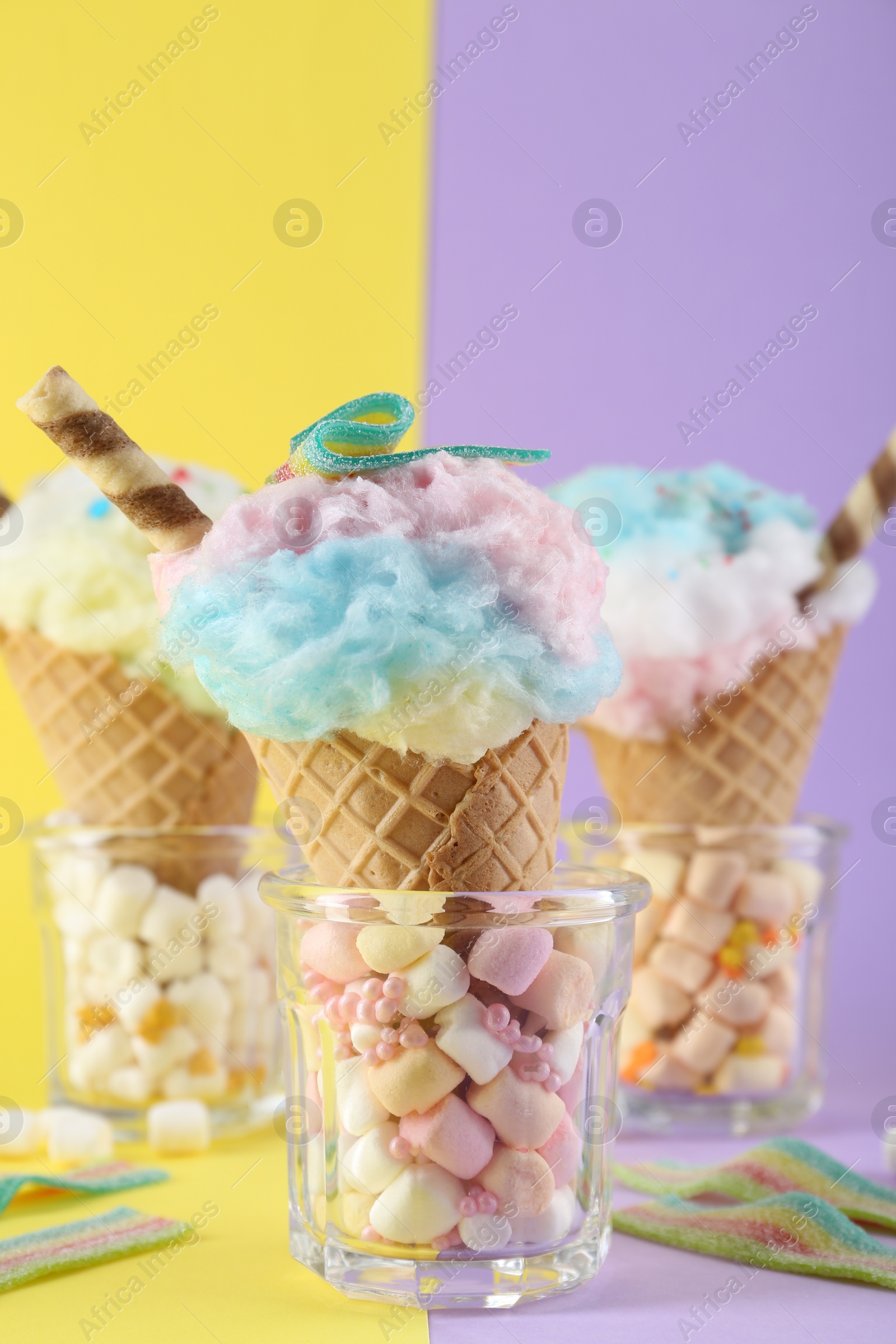 Photo of Sweet cotton candies in waffle cones and marshmallows on color background, closeup