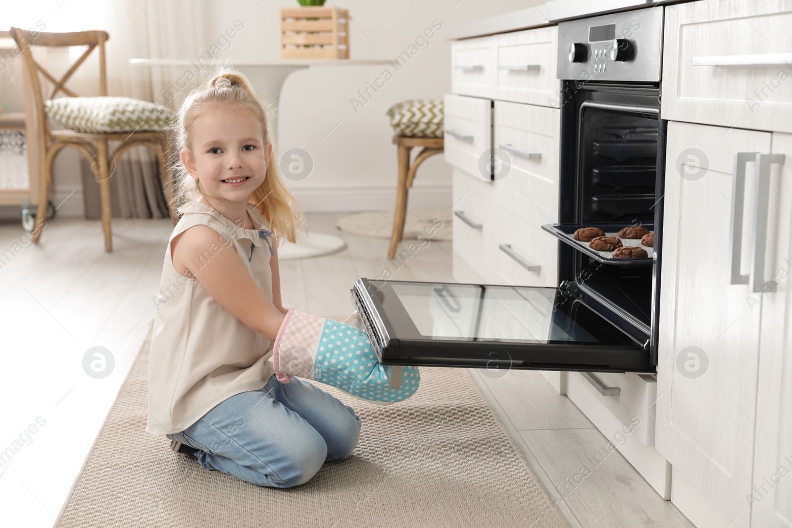 Photo of Little girl opening door of oven with cookies in kitchen