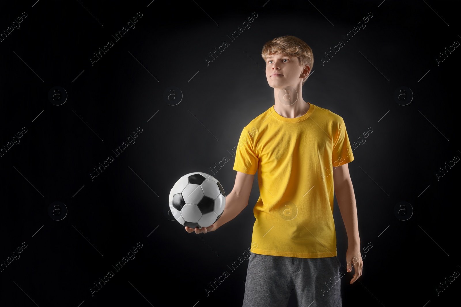 Photo of Teenage boy with soccer ball on black background. Space for text