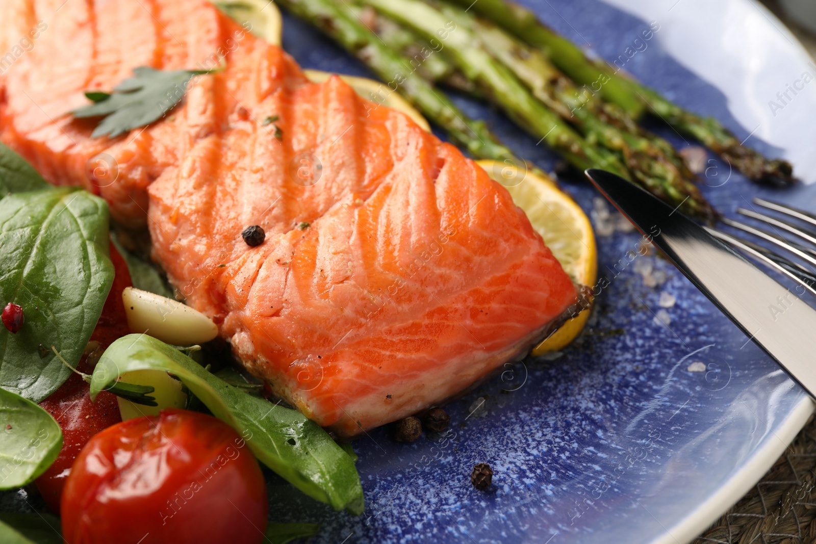 Photo of Tasty grilled salmon with tomatoes, asparagus, spinach and spices on plate, closeup