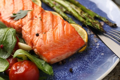 Tasty grilled salmon with tomatoes, asparagus, spinach and spices on plate, closeup