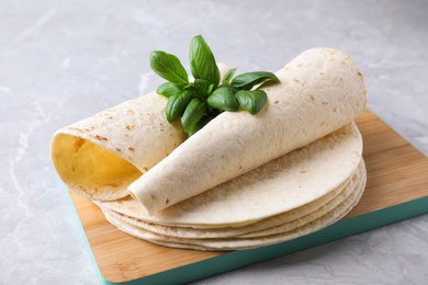 Photo of Board of tasty tortillas with basil leaves on grey table, closeup