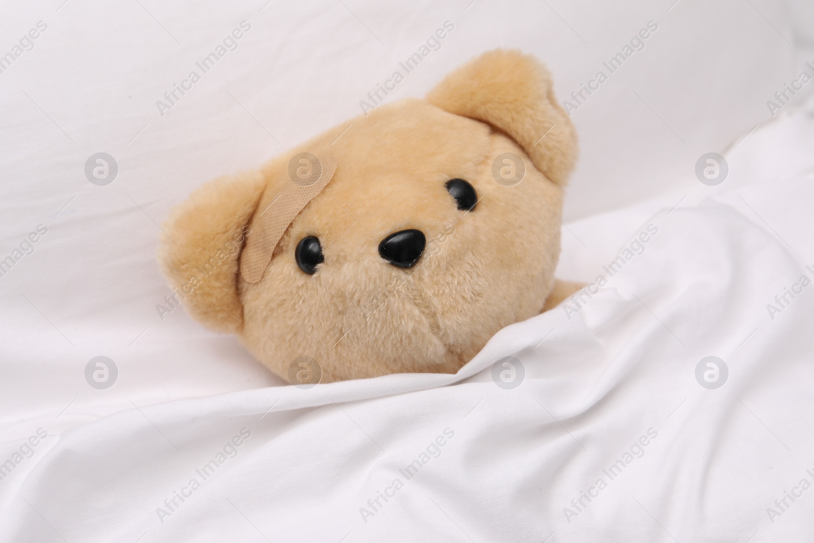 Photo of Toy cute bear with sticking plaster under blanket in bed