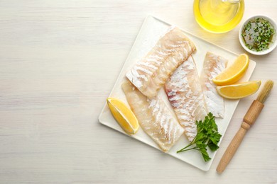 Photo of Fresh raw cod fillets with spices and lemon on white wooden table, flat lay. Space for text