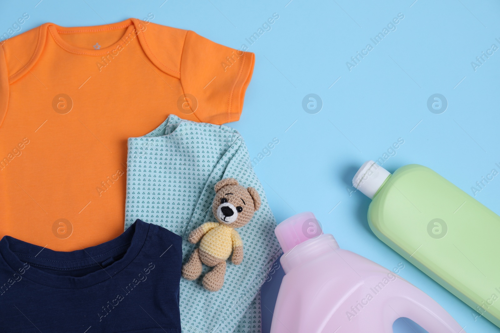 Photo of Bottles of laundry detergents, baby clothes and toy bear on light blue background, flat lay. Space for text