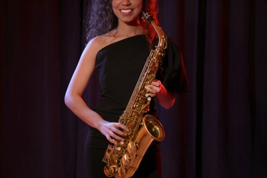 Photo of African American woman with saxophone on dark background, closeup