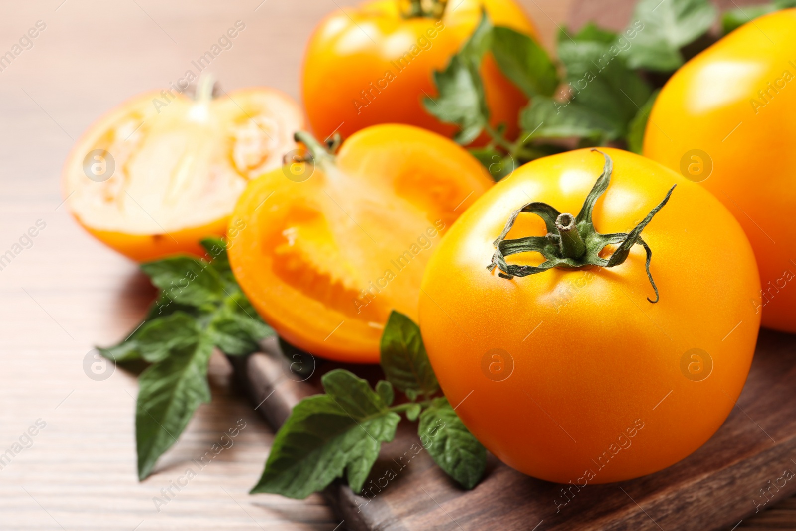 Photo of Fresh ripe yellow tomatoes with leaves on wooden table, closeup