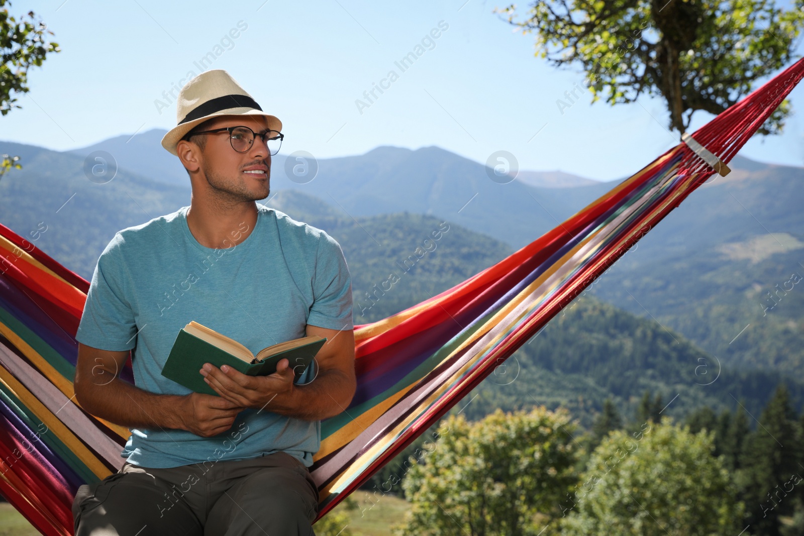 Photo of Handsome man reading book in hammock outdoors on sunny day