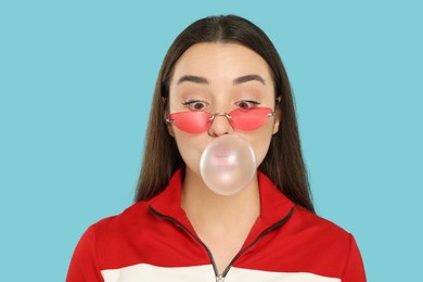 Beautiful young woman blowing bubble gum on light blue background