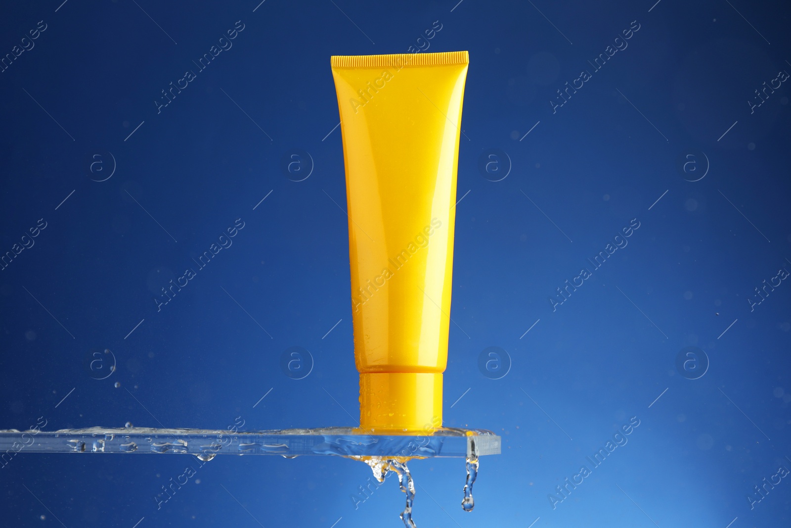 Photo of Moisturizing cream in tube on glass with water drops against blue background. Space for text