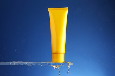 Moisturizing cream in tube on glass with water drops against blue background. Space for text