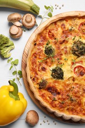 Delicious homemade vegetable quiche and ingredients on white table, flat lay