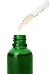 Essential oil dripping from pipette into glass bottle on white background