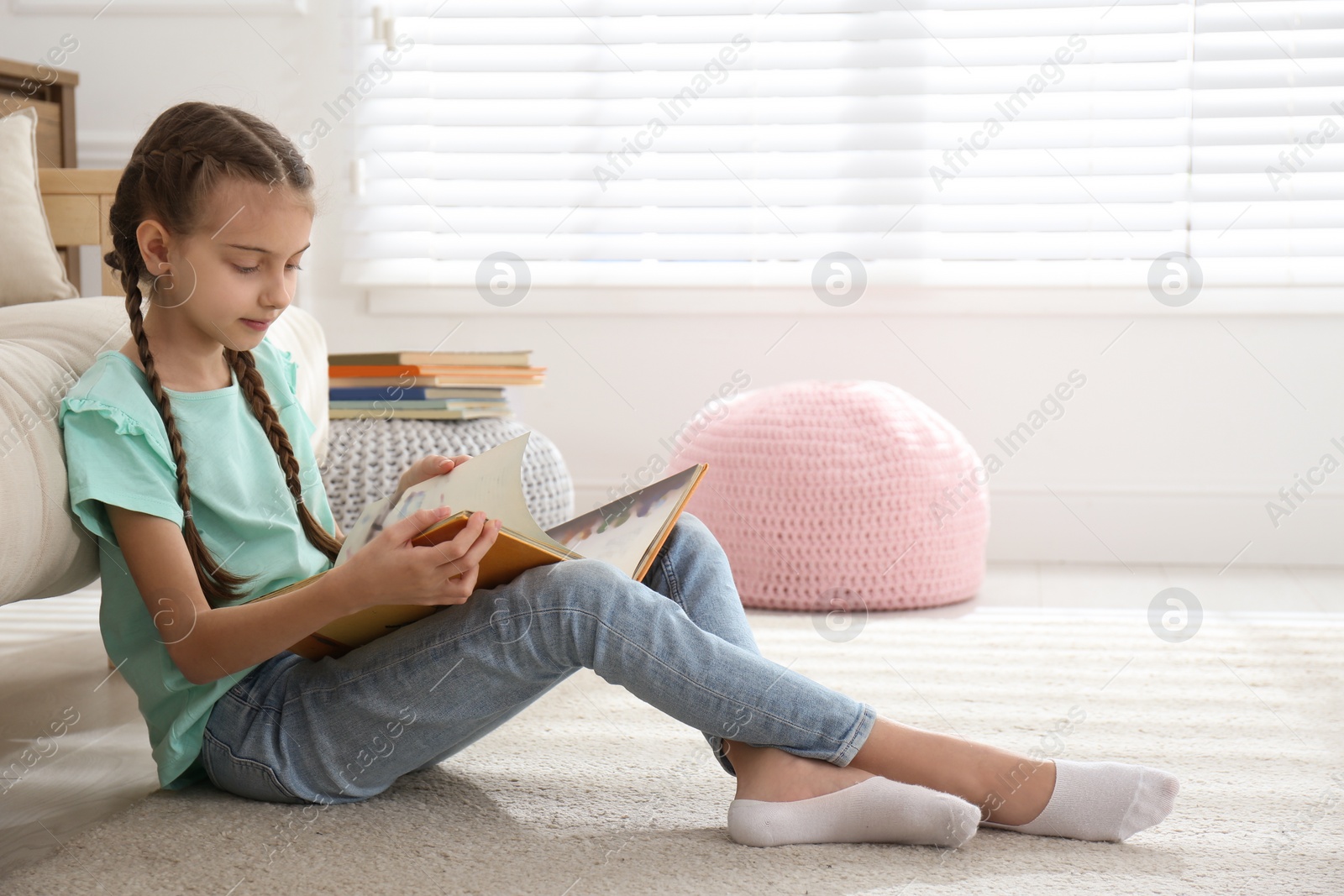 Photo of Cute little girl reading book on floor at home