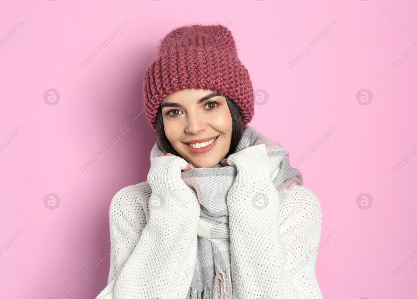 Photo of Young woman wearing warm sweater, scarf and hat on pink background. Winter season