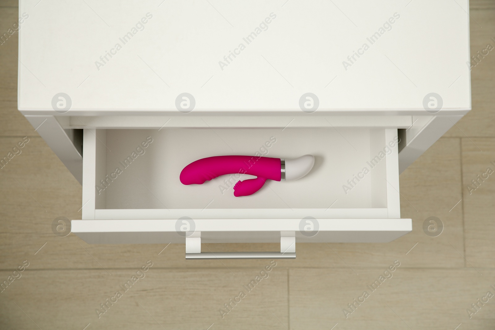 Photo of Pink vaginal vibrator in drawer indoors, top view. Sex toy