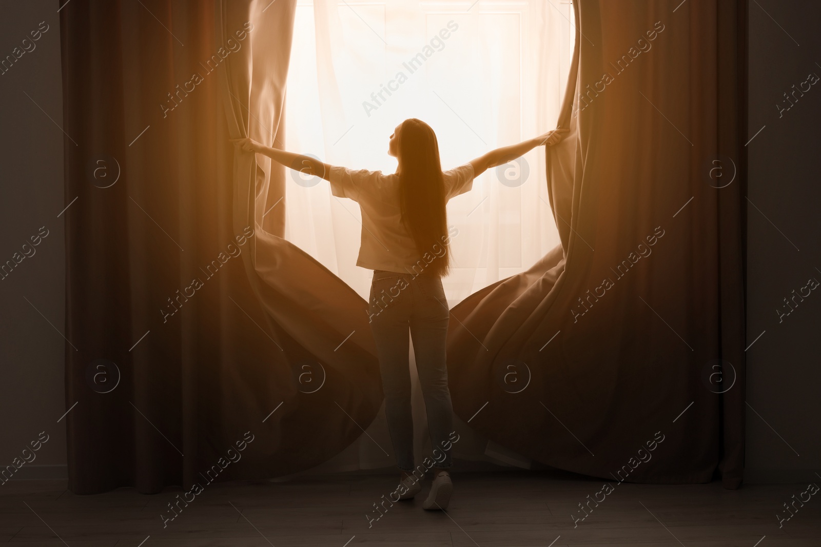 Photo of Woman opening stylish curtains at home, back view