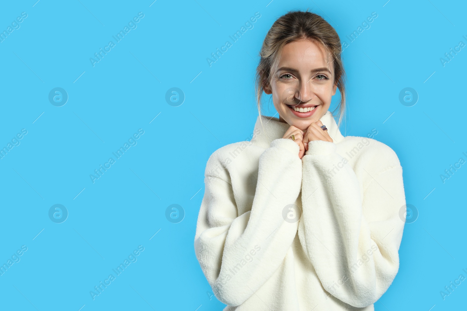 Photo of Beautiful young woman wearing knitted sweater on light blue background. Space for text